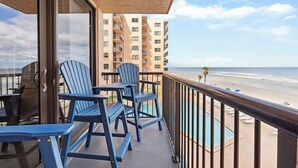 Un balcon avec des fauteuils Adirondack bleus, une piscine et une vue sur la plage et l’océan.
