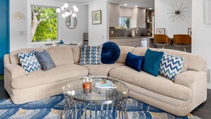 Een moderne woonkamer met een beige modulaire bank, een glazen salontafel en een blauw tapijt met patroon.