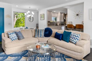 A modern living room with a beige sectional sofa, a glass coffee table, and a blue patterned rug.