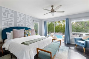 A bedroom with a large bed, a ceiling fan, a view of a swimming pool, and a balcony.