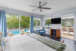 A bedroom with a bed, a ceiling fan, a TV, a desk, and a view of a swimming pool.