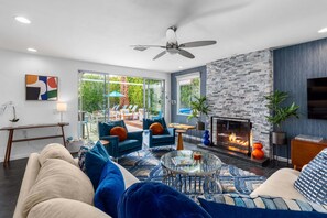 A modern living room with a fireplace, comfortable seating, and a large window overlooking a garden. - Sapphire Hideaway - Palm Springs Retreat (Palm Springs)