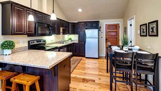 A kitchen with dark wood cabinets, a granite countertop, a stainless steel refrigerator, and a wooden dining area with chairs. - Bluebird Day - Twin Mills Bungalow in Bend, OR, featuring 2 cozy bedrooms. (Bend)