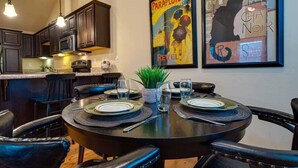 A dining area with a round table set for four, surrounded by black leather chairs. There are plates, glasses, and a small potted plant on the table. - Bluebird Day - Sierra Nook, one-bedroom retreat in Bend, ideal for couples and pet-friendly. (Bend)