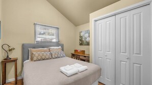 A bedroom with a bed, a nightstand, a window with blinds, a painting, and a wardrobe. - Bluebird Day - Sierra Nook, one-bedroom retreat in Bend, ideal for couples and pet-friendly. (Bend)