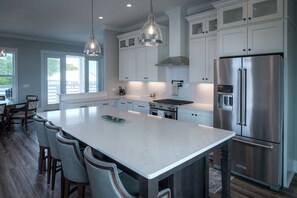 Una cocina moderna con armarios blancos, una isla grande, electrodomésticos de acero inoxidable e iluminación colgante.