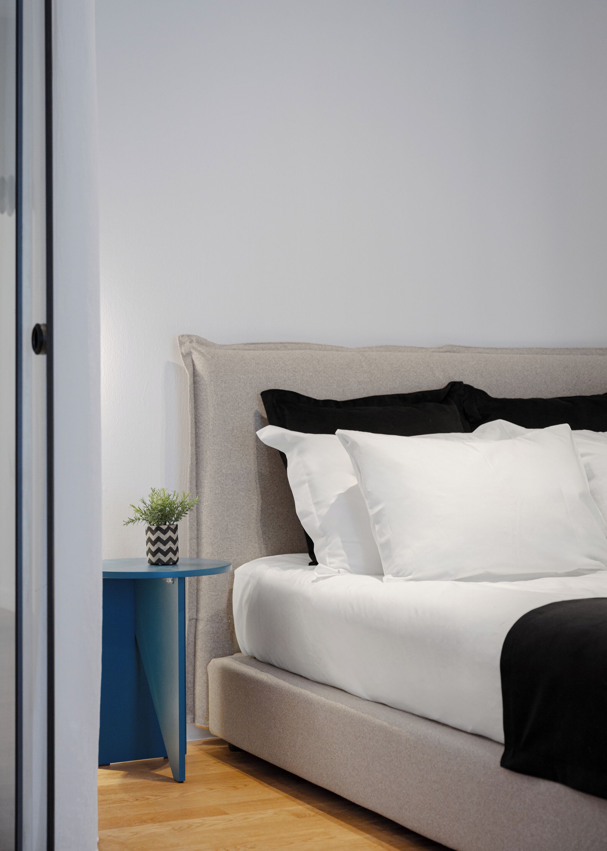 A bedroom with a bed, a small side table, and a potted plant.