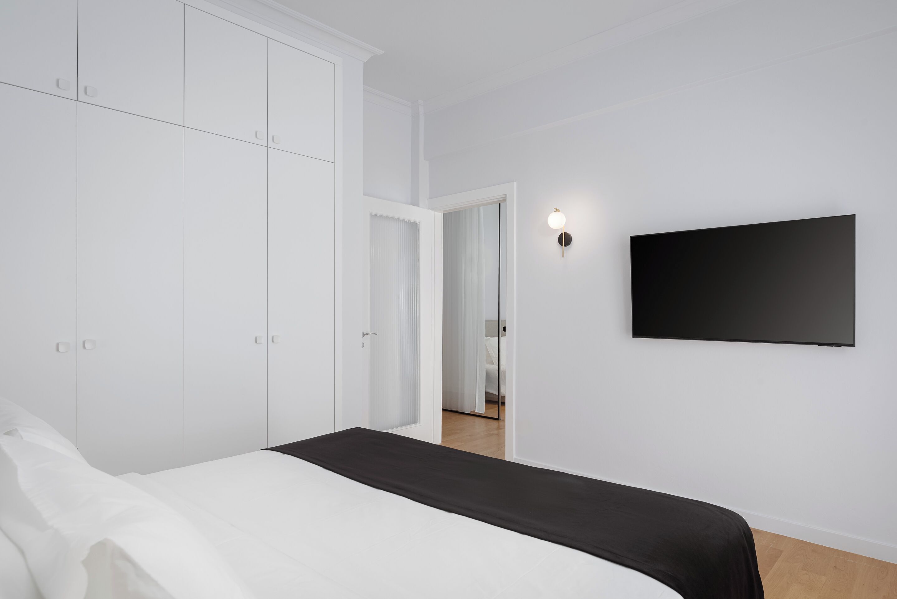 A bedroom with a bed, white wardrobe, and a wall-mounted TV.