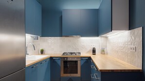 A modern kitchen with blue cabinets, a stainless steel refrigerator, a white sink, and a wooden countertop. - Acropolis Classy Apartments (Athens)