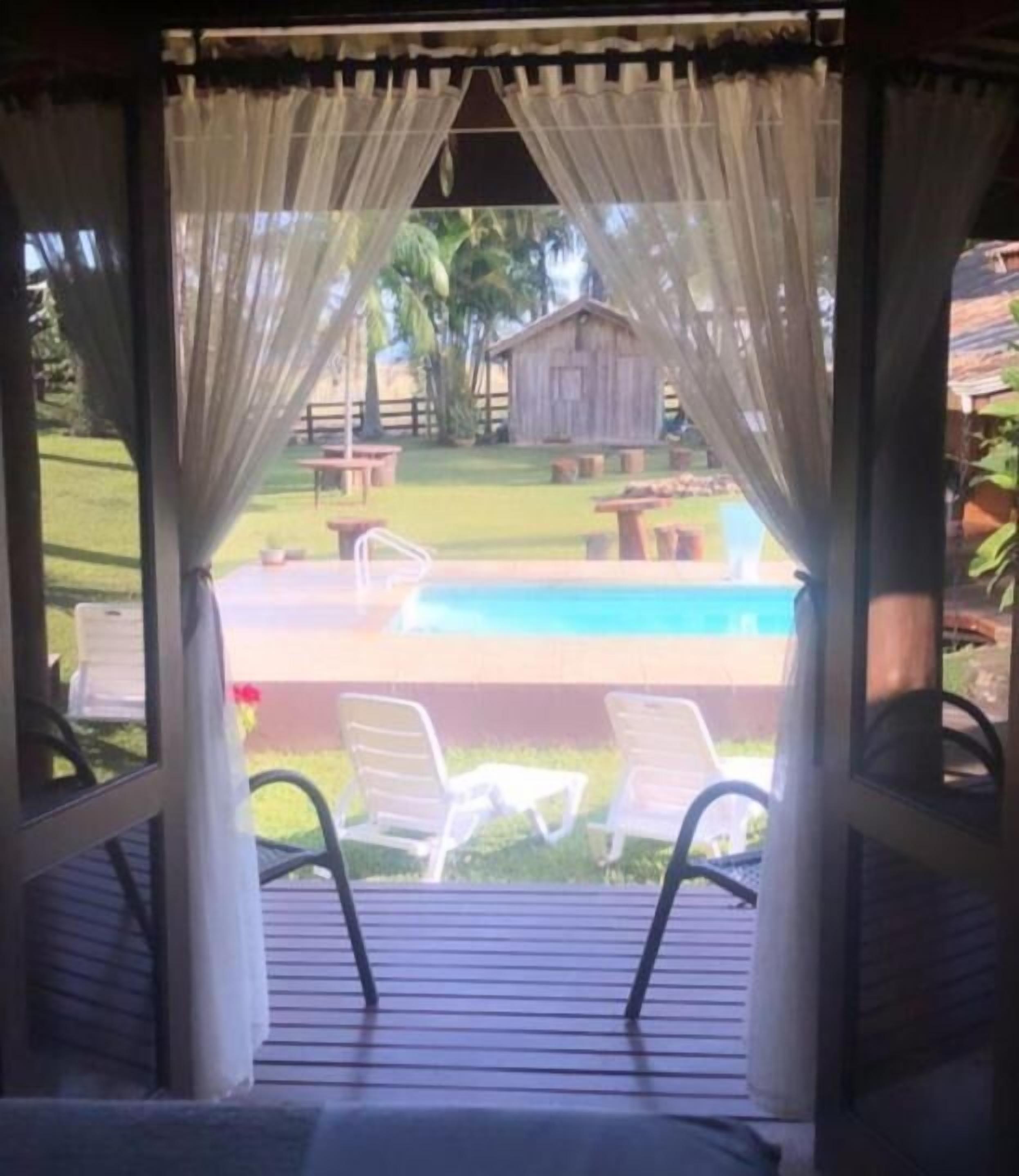 A covered outdoor seating area with a pool view, featuring a wooden deck and two lounge chairs.
