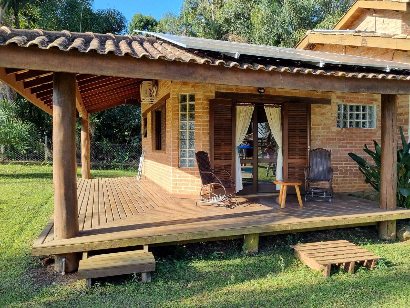 Une terrasse en bois avec un espace patio couvert, un bâtiment en briques doté d’une porte en verre et un petit coin salon extérieur avec deux chaises.