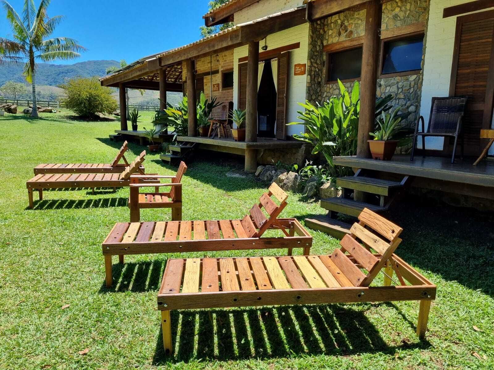 Un patio con sillones de madera y un edificio de piedra con un porche cubierto.