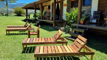 Un patio con sillones de madera y un edificio de piedra con un porche cubierto.