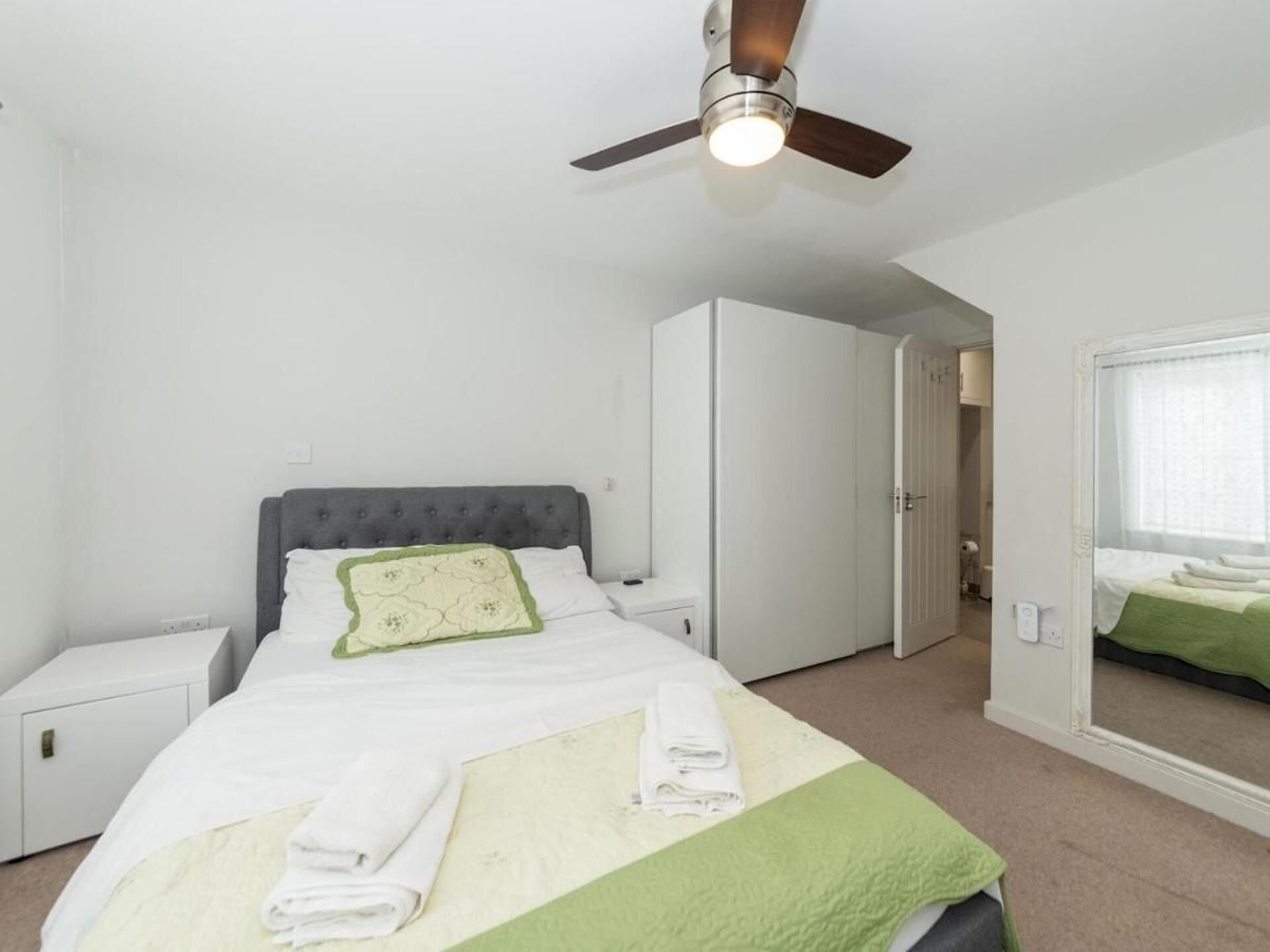 Een slaapkamer met een bed, nachtkastje, kledingkast, plafondventilator en een raam met uitzicht.