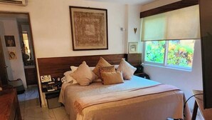 A hotel room with a bed, a ceiling fan, a window with a view of greenery, and a TV on a wooden stand. - Luxury on stunning La Ropa beach in tropical Zihuatanejo Mexico (Zihuatanejo México)