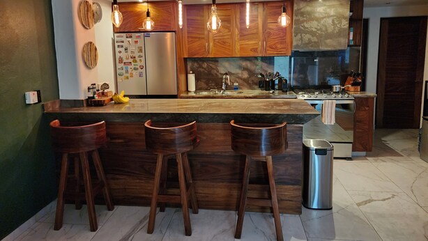 A modern kitchen with wooden cabinets, a marble countertop, and a central island with bar stools. - Luxury on stunning La Ropa beach in tropical Zihuatanejo Mexico (Zihuatanejo México)