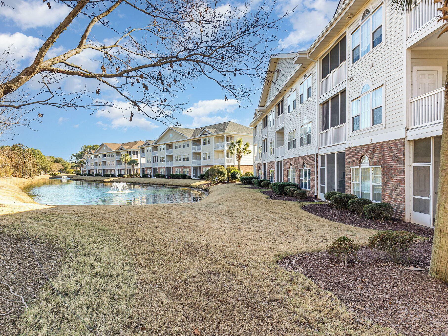 A multi-story residential building with a swimming pool, a grassy area, and a small pond.