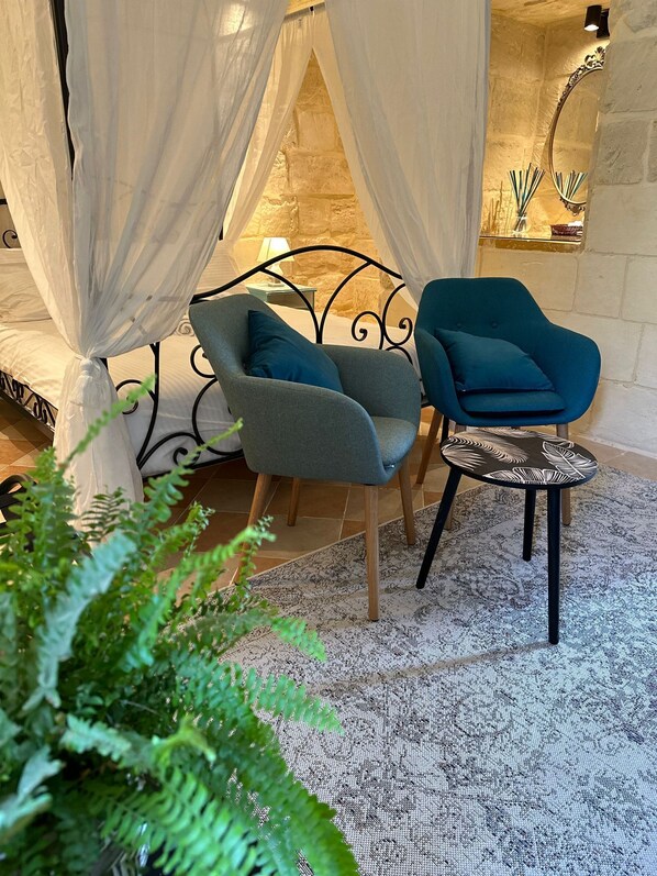 Una habitación acogedora con una cama, dos sillas, una mesita y una planta grande.