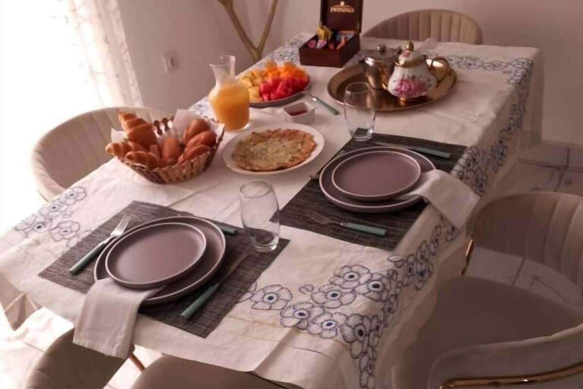 A dining table set with plates, cutlery, a fruit bowl, and a teapot.