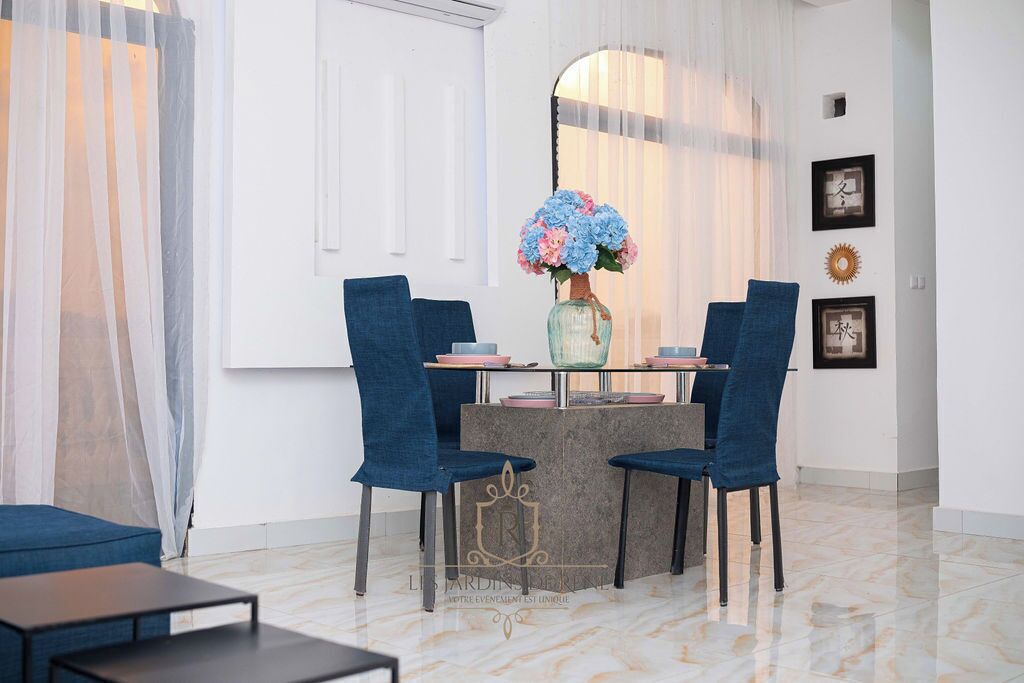 Un coin repas avec une table dressée pour quatre personnes, agrémenté de chaises bleues et d’un vase rempli de fleurs.