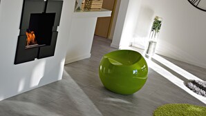 Een modern interieur met een ingebouwde open haard, een groene bolvormige fauteuil en een minimalistische inrichting.