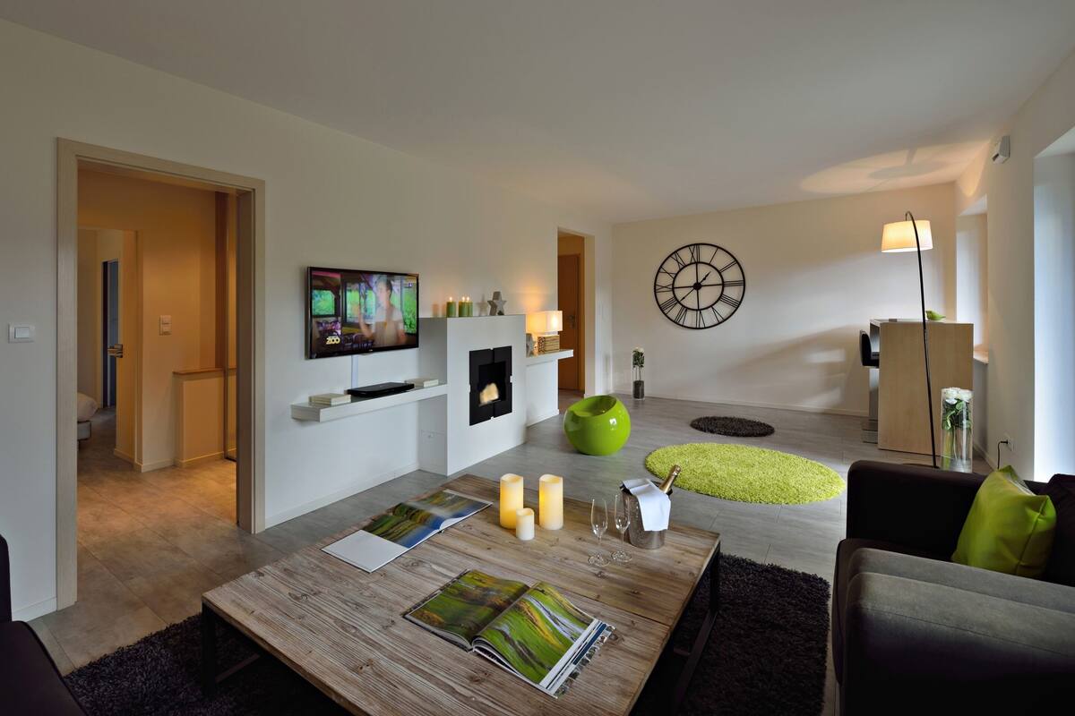 Una sala de estar moderna con un televisor de pantalla plana, una chimenea, un reloj y una butaca verde.