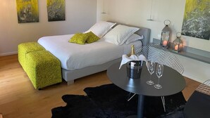 Een moderne slaapkamer met een bed, een rond tafeltje met een fles en glazen, en kunstwerken aan de wanden.