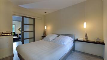 A modern bedroom with a large bed, a nightstand with a lamp, and a small decorative tree on the nightstand.