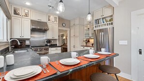 A modern kitchen with white cabinets, stainless steel appliances, and a central island with orange placemats.