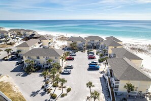 Un hotel frente a la playa con varias construcciones, un estacionamiento y vista al océano.