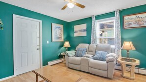A living room with teal walls, a beige sofa, a wooden coffee table, and a ceiling fan.