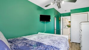 A bedroom with a bed, a ceiling fan, a TV mounted on the wall, and a door leading to a bathroom.