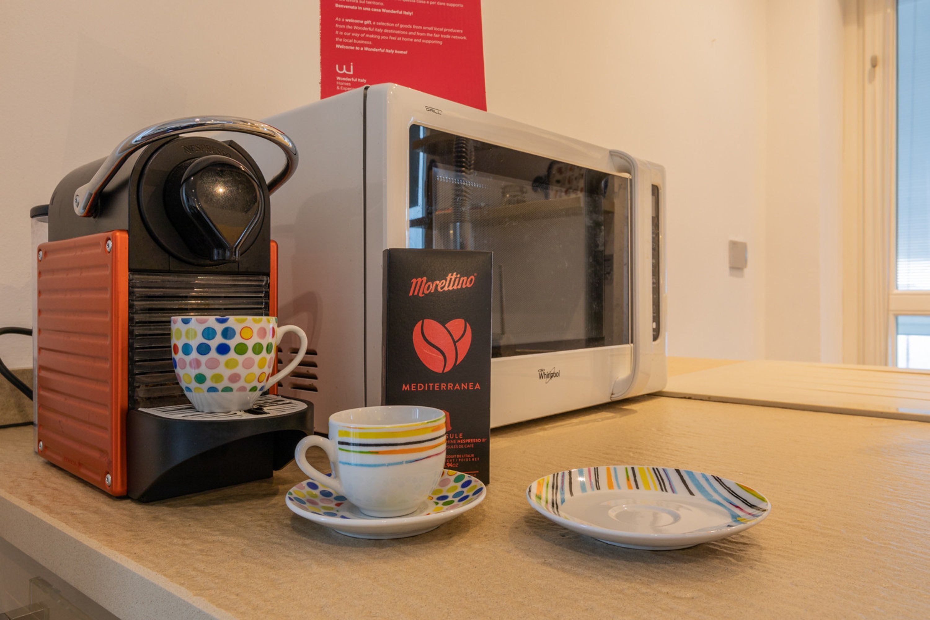 A coffee machine with a cup and saucer, a microwave, and a plate on a countertop.