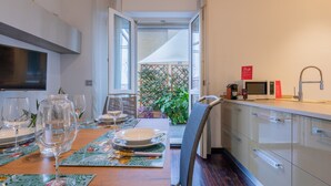 Ein Essbereich mit Holztisch, gedeckt für eine Mahlzeit, eine Küche mit modernen Geräten und Blick auf einen Garten durch eine offene Tür.