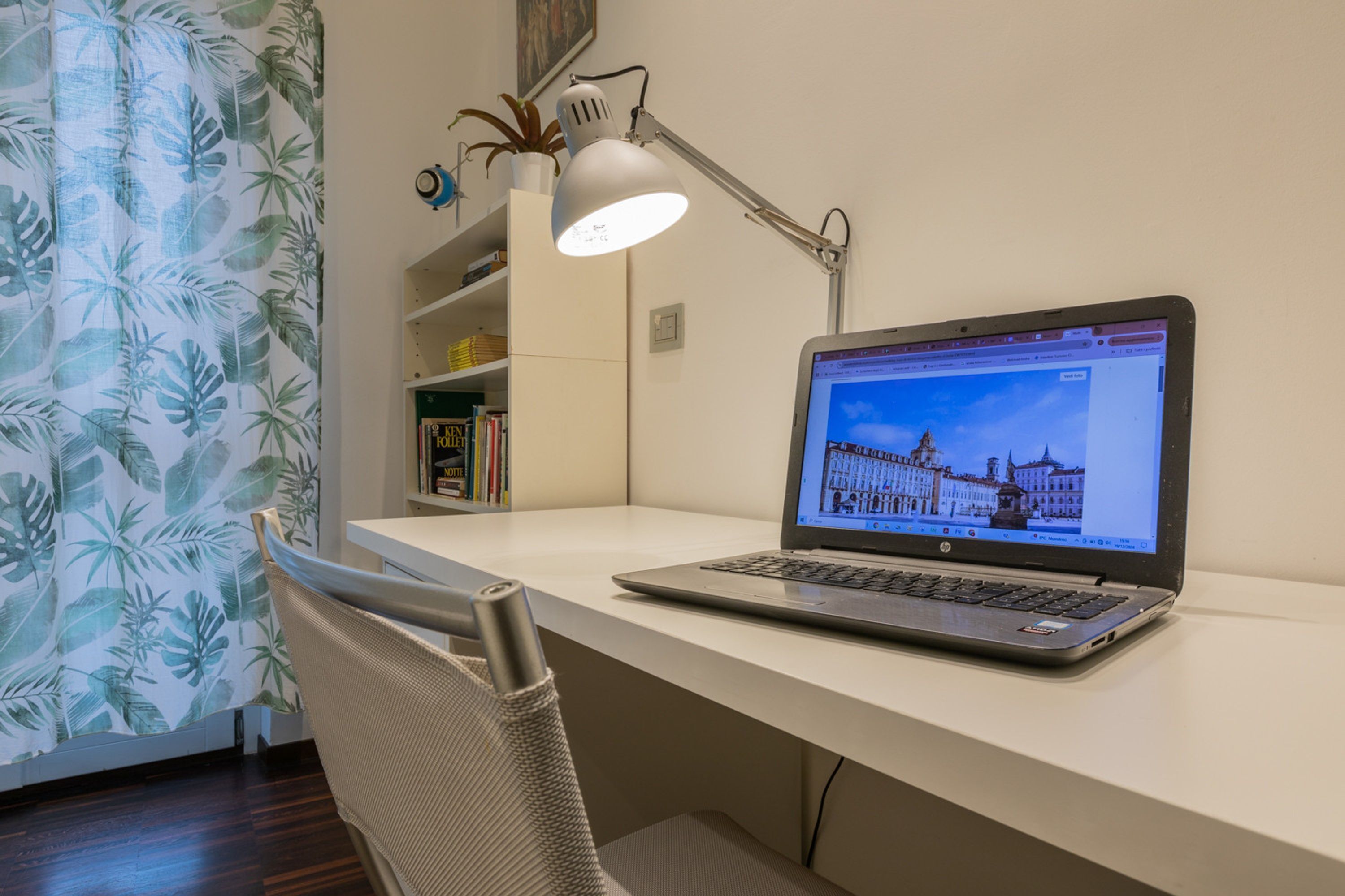 A laptop on a desk with a white lamp and a bookshelf in the background.