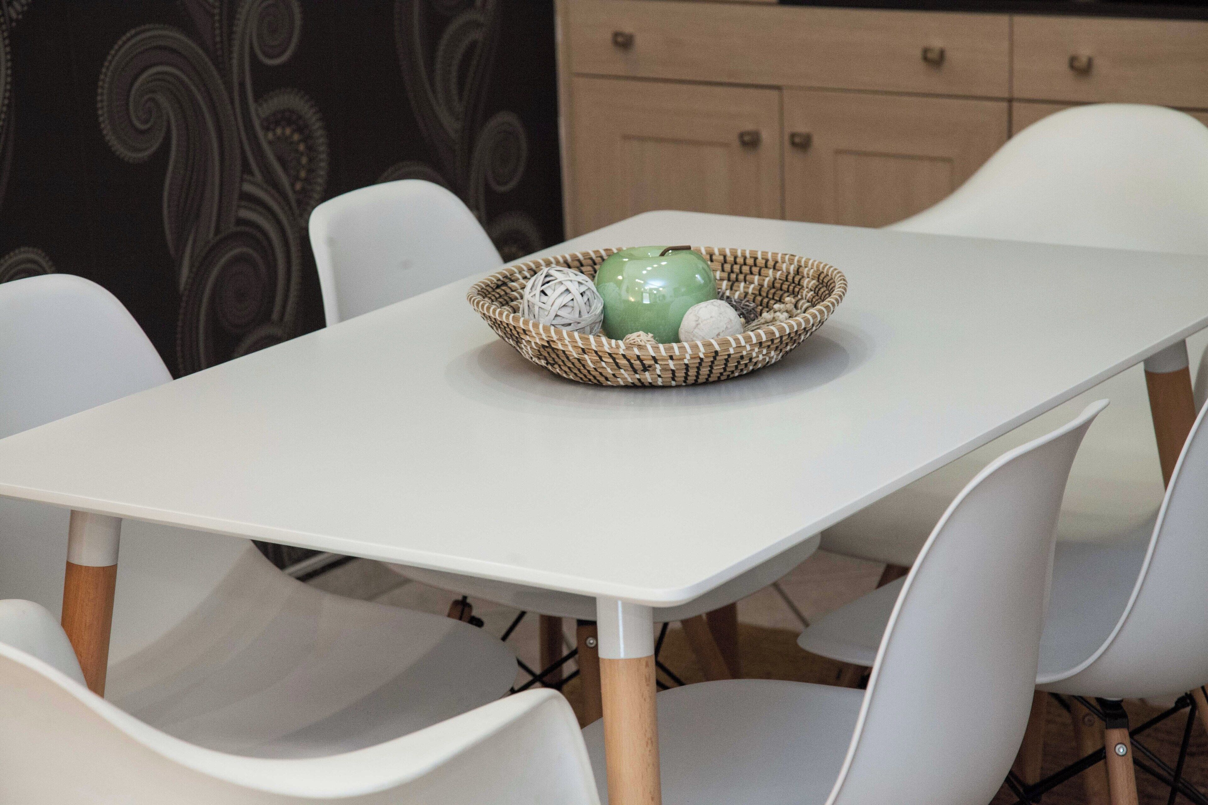 Una mesa de comedor con una cesta tejida que contiene una manzana verde, un objeto blanco y esférico, y una trufa de chocolate.