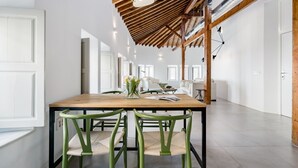 A spacious room with a wooden ceiling, a dining table with chairs, and a white wall with a door.