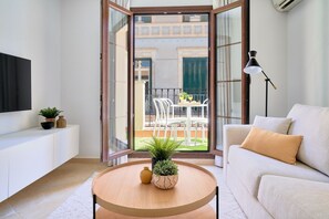 Un salon moderne avec un canapé, une table ronde agrémentée d’une plante et un téléviseur posé sur un meuble blanc.