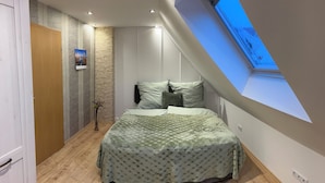 A bedroom with a sloped ceiling and skylight, a bed with a patterned bedspread, a small plant, and a wall-mounted photo. - Vacation home "Green Emotion" (Suhl)