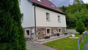 A two-story house with a red-tiled roof, stone foundation, and a paved driveway. - Vacation home "Green Emotion" (Suhl)