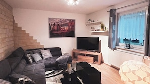 A modern living room with a sectional sofa, a flat-screen TV, and a staircase. - Vacation home "Green Emotion" (Suhl)