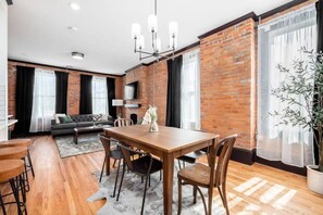 Un salon moderne avec un mur en briques, un canapé, une table à manger avec des chaises et une grande plante.
