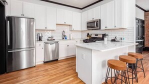 A modern kitchen with white cabinetry, stainless steel appliances, a marble island, and wooden flooring. - OSU & Crew Stadium | Easy Walk | Great Design (Columbus)