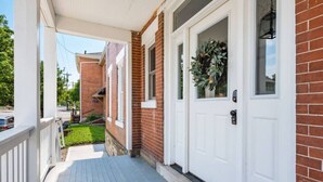 A covered porch with a white door and a wreath, leading to a brick house. - OSU & Crew Stadium | Easy Walk | Great Design (Columbus)