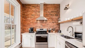 A kitchen with white cabinets, a stainless steel oven, a brick wall, and a window. - Access OSU & Crew Stadium | Pet Friendly | Parking (Columbus)