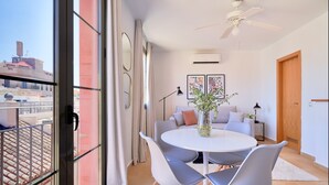 A modern dining area with a round table and grey chairs, a ceiling fan, and a view of the city through large windows.
