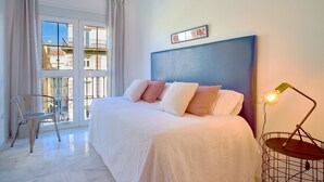 Ein Schlafzimmer mit einem großen Bett, einem Sessel, einer Nachttischlampe und einem Fenster mit Vorhängen.