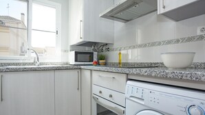 Une cuisine moderne avec des meubles blancs, un four à micro-ondes encastré, un lave-linge et un plan de travail en granit.