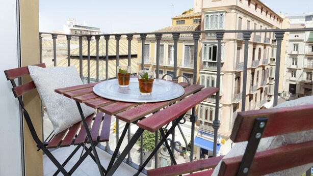Un balcon avec une table ronde et deux chaises, donnant sur un paysage urbain parsemé de bâtiments historiques.
