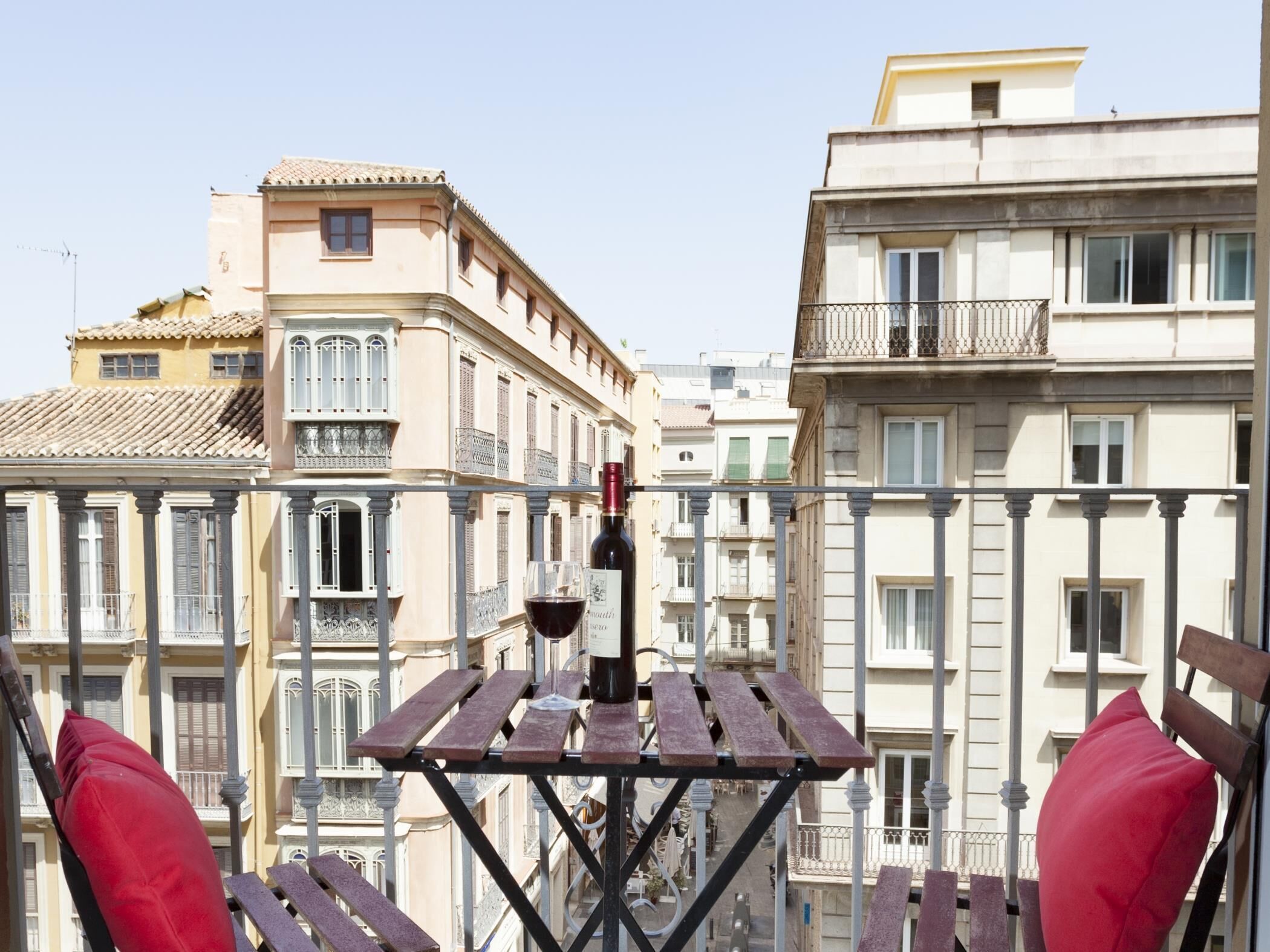 Ein Balkon mit Tisch, roten Kissen und einer Weinflasche.